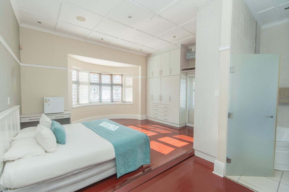 Spacious bedroom featuring a coffered ceiling, built-in cabinetry, a bay window, and an integrated en-suite bathroom with a frosted glass door.