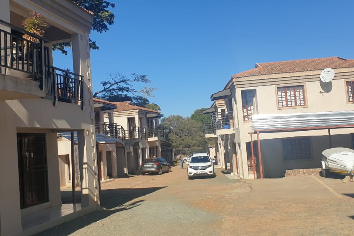 Exterior view of a townhouse complex featuring multiple units with balconies, tiled roofs, and a shared paved driveway with carport parking.