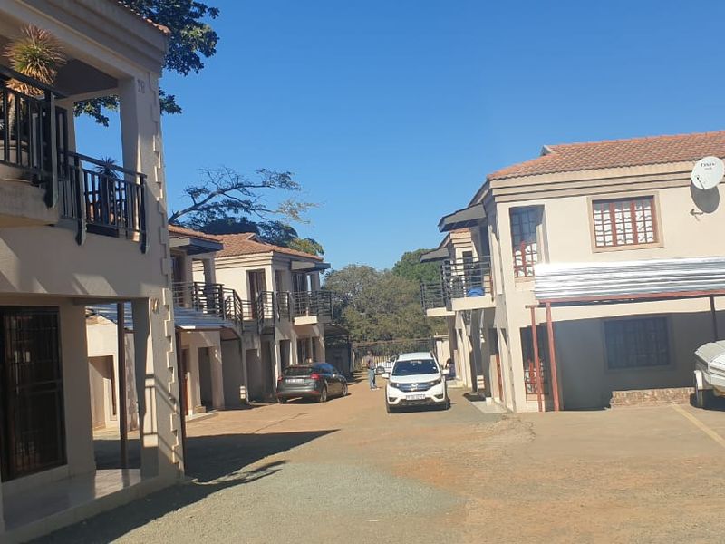 Exterior view of a townhouse complex featuring multiple units with balconies, tiled roofs, and a shared paved driveway with carport parking.