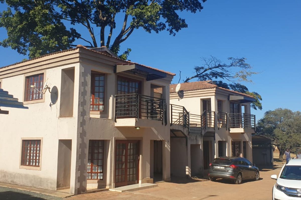 Front elevation of a two-story townhouse complex featuring tiled roofs, private balconies with metal railings, and a paved driveway area.