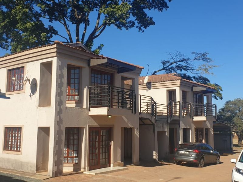 Front elevation of a two-story townhouse complex featuring tiled roofs, private balconies with metal railings, and a paved driveway area.