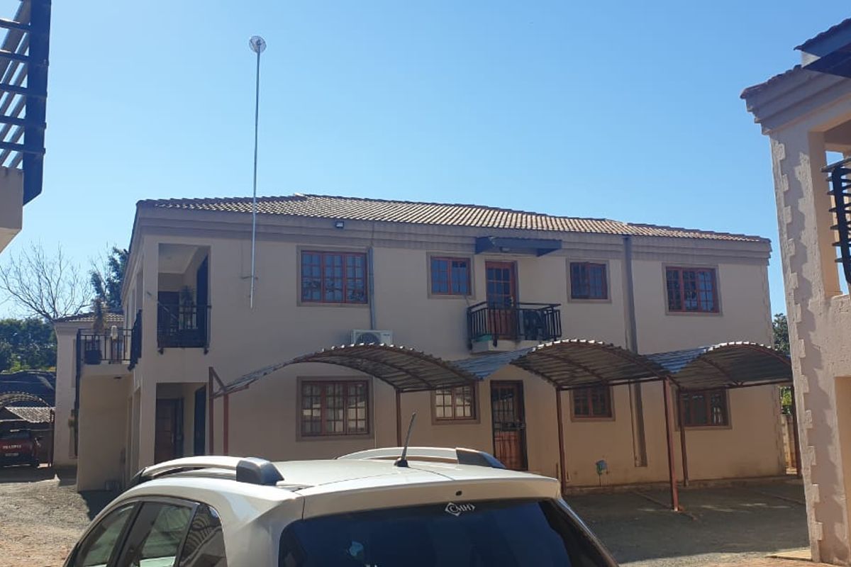 Rear view of a multi-story townhouse complex featuring tiled roofing, private balconies, and covered carport parking bays.