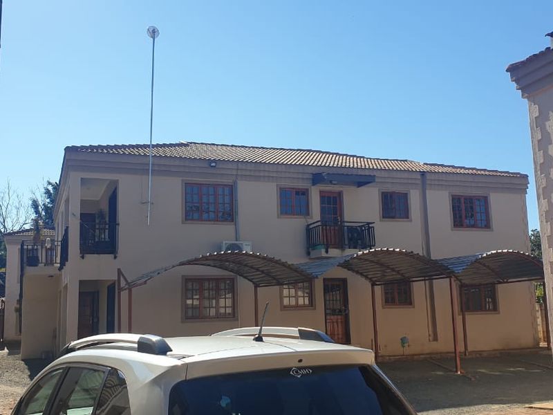 Rear view of a multi-story townhouse complex featuring tiled roofing, private balconies, and covered carport parking bays.