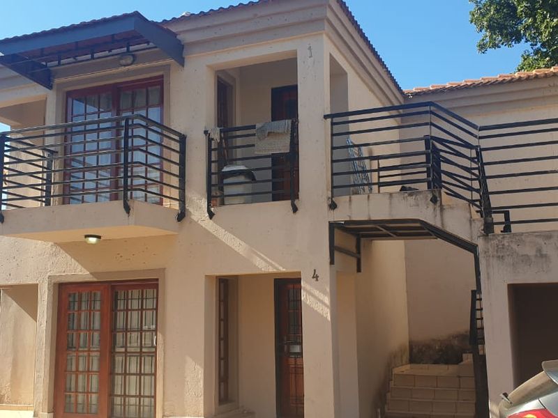 Front elevation of a two-story townhouse featuring a balcony, external staircase, and metal railings with visible exterior wall weathering.