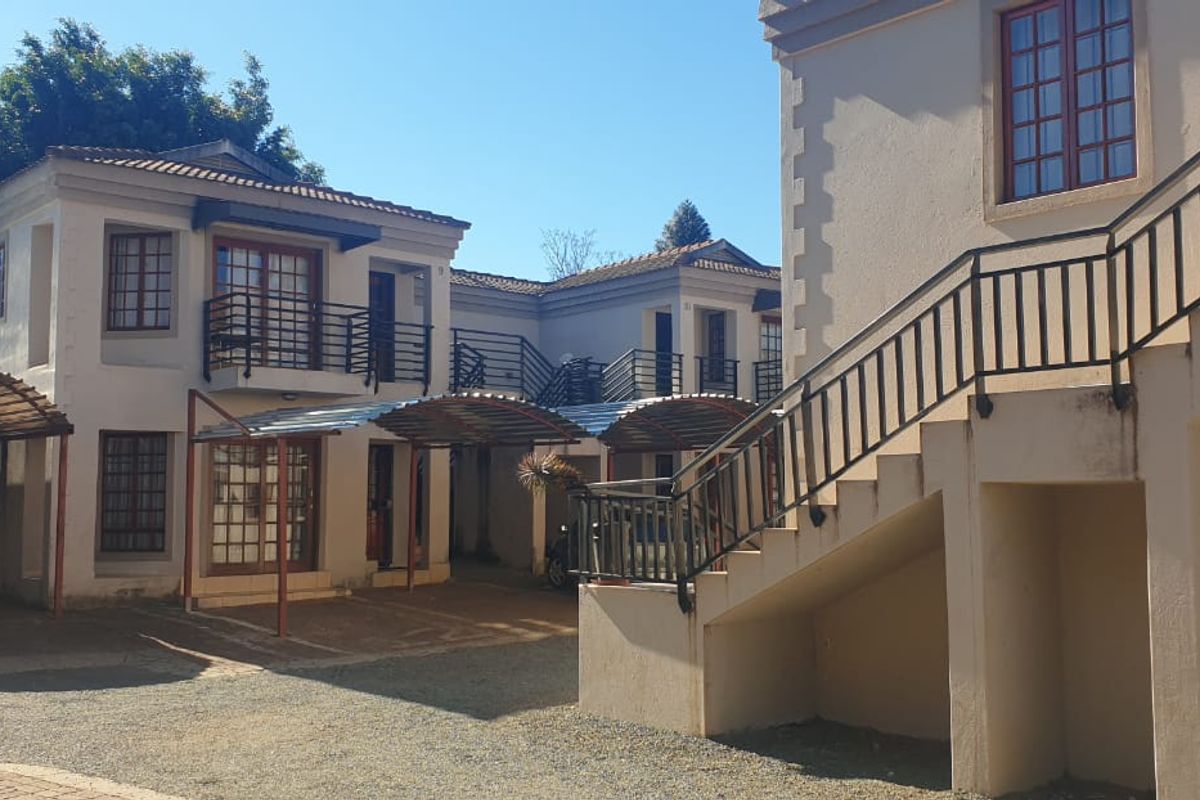Exterior view of a townhouse complex featuring multi-level units with external staircases, covered carports, and traditional casement windows.