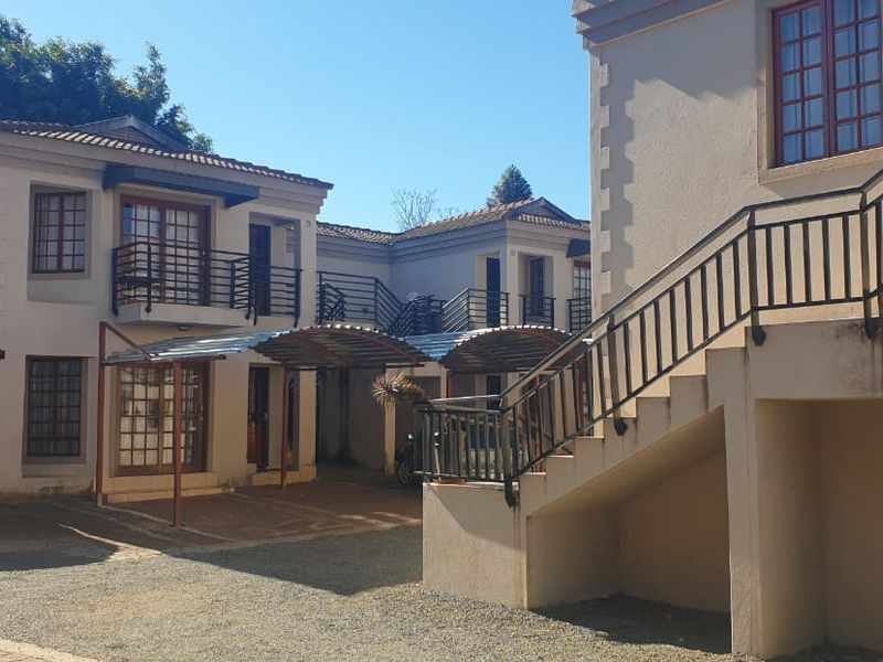 Exterior view of a townhouse complex featuring multi-level units with external staircases, covered carports, and traditional casement windows.