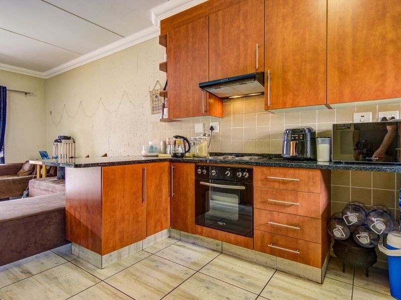 Open-plan kitchen featuring wood-finish cabinetry, granite countertops, and integrated appliances, flowing into the adjacent living area with tiled flooring throughout.