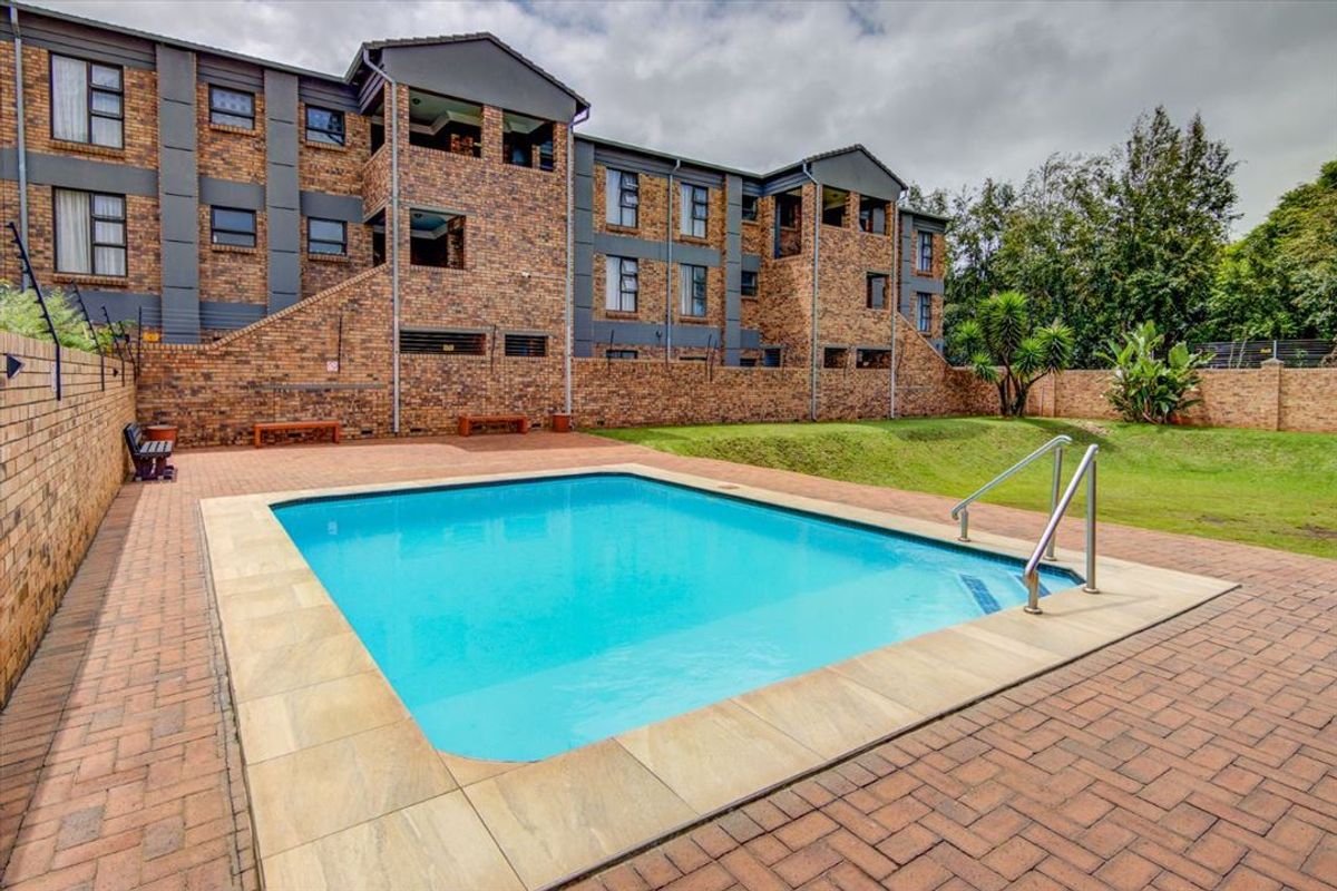 Communal swimming pool area featuring brick paving, a pool ladder, and surrounding lawn within a secure townhouse complex.