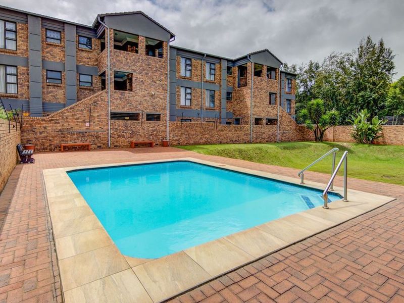 Communal swimming pool area featuring brick paving, a pool ladder, and surrounding lawn within a secure townhouse complex.