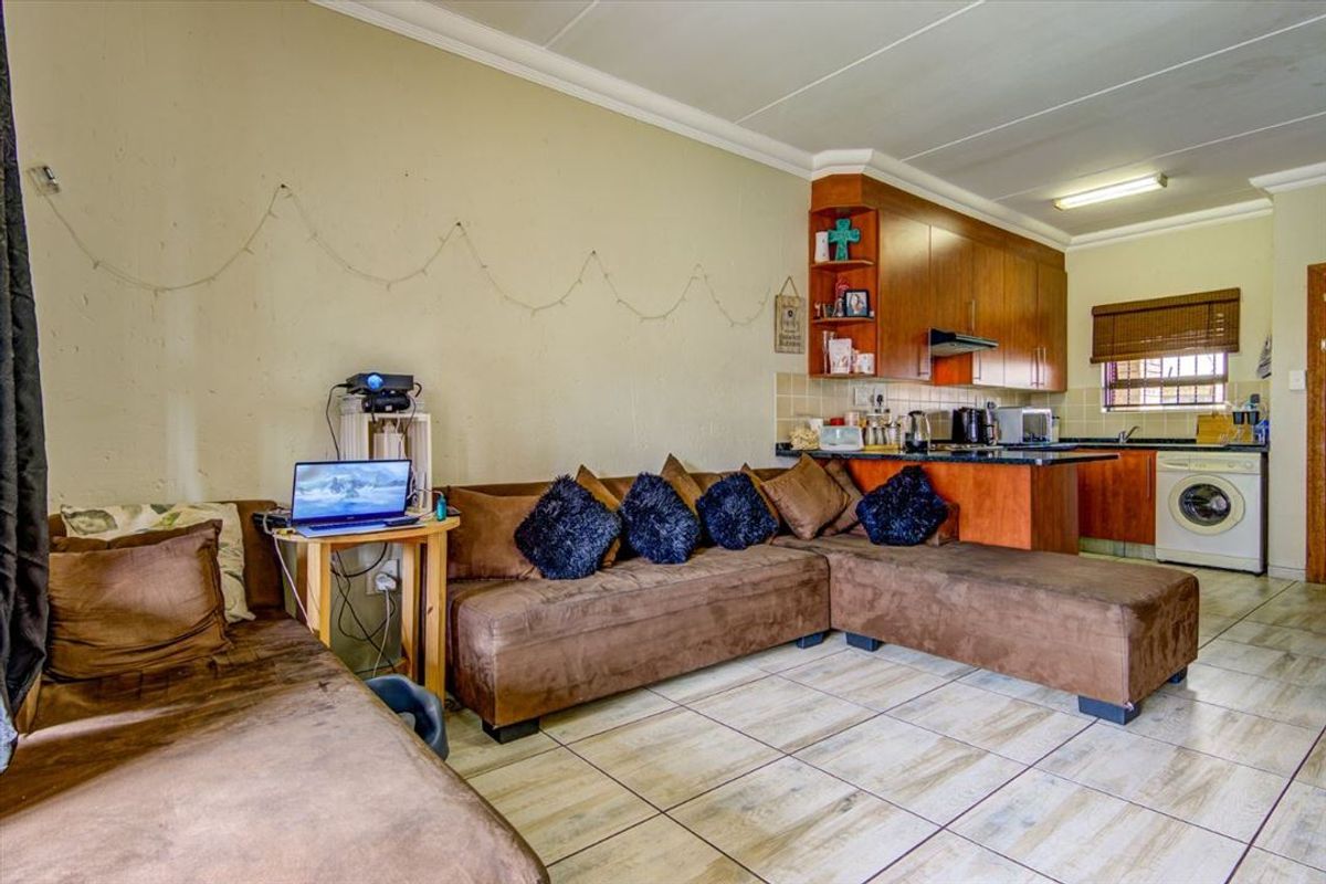 Open-plan living area featuring tiled flooring and a compact kitchen with built-in cabinetry and integrated laundry appliance space.