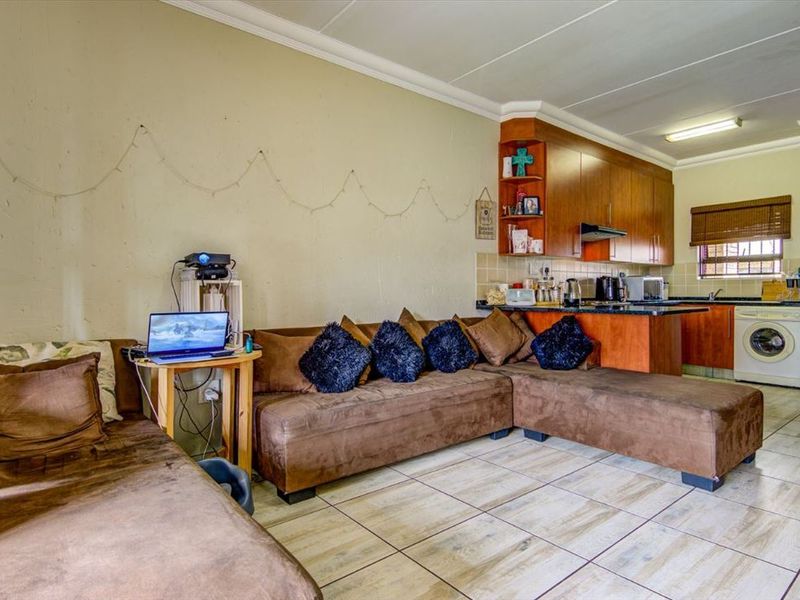 Open-plan living area featuring tiled flooring and a compact kitchen with built-in cabinetry and integrated laundry appliance space.