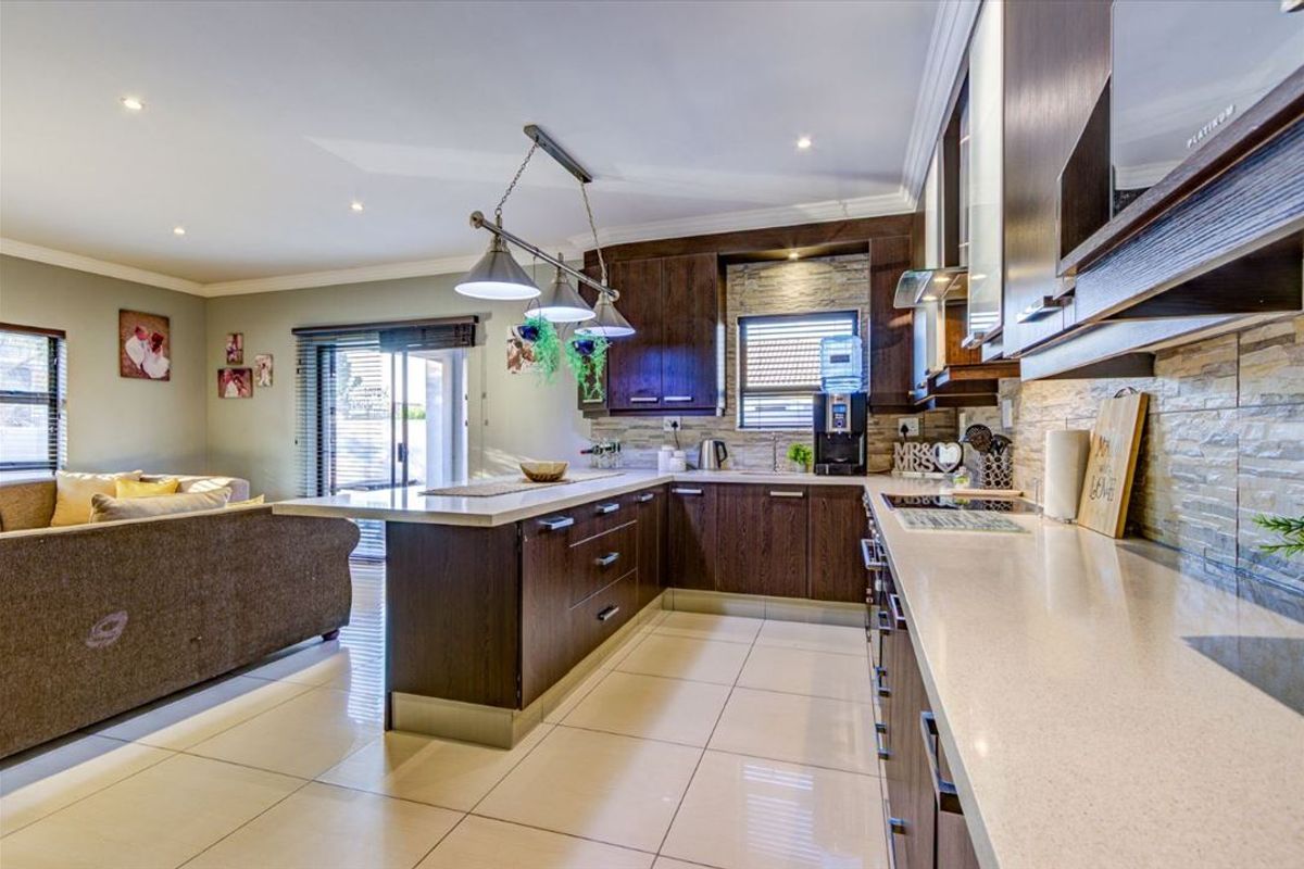 Open-plan kitchen featuring dark wood cabinetry, stone-cladding backsplash, stone countertops, and recessed lighting, seamlessly flowing into the adjacent living area.
