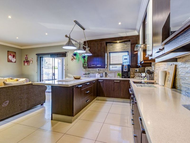 Open-plan kitchen featuring dark wood cabinetry, stone-cladding backsplash, stone countertops, and recessed lighting, seamlessly flowing into the adjacent living area.