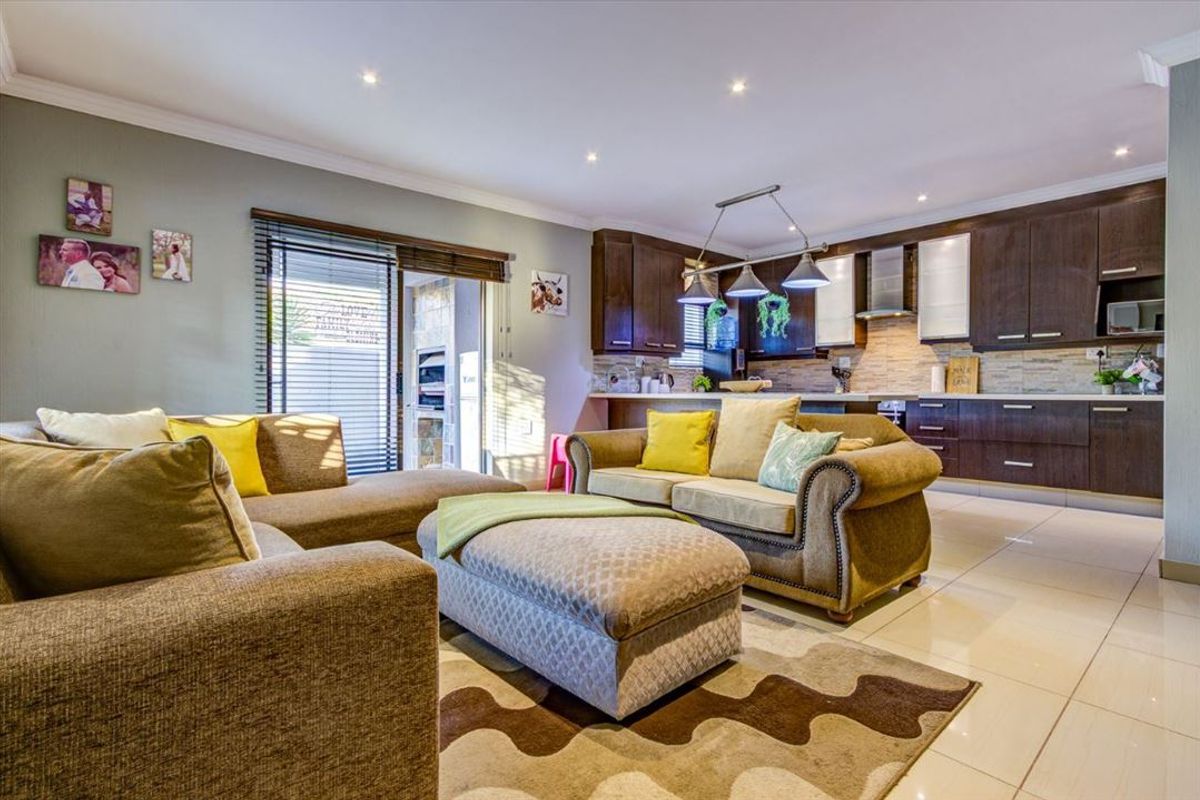Open-plan living area featuring a modern kitchen with dark wood cabinetry, stone-tiled backsplash, and integrated lighting, flowing into a comfortable lounge space.