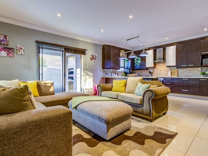 Open-plan living area featuring a modern kitchen with dark wood cabinetry, stone-tiled backsplash, and integrated lighting, flowing into a comfortable lounge space.