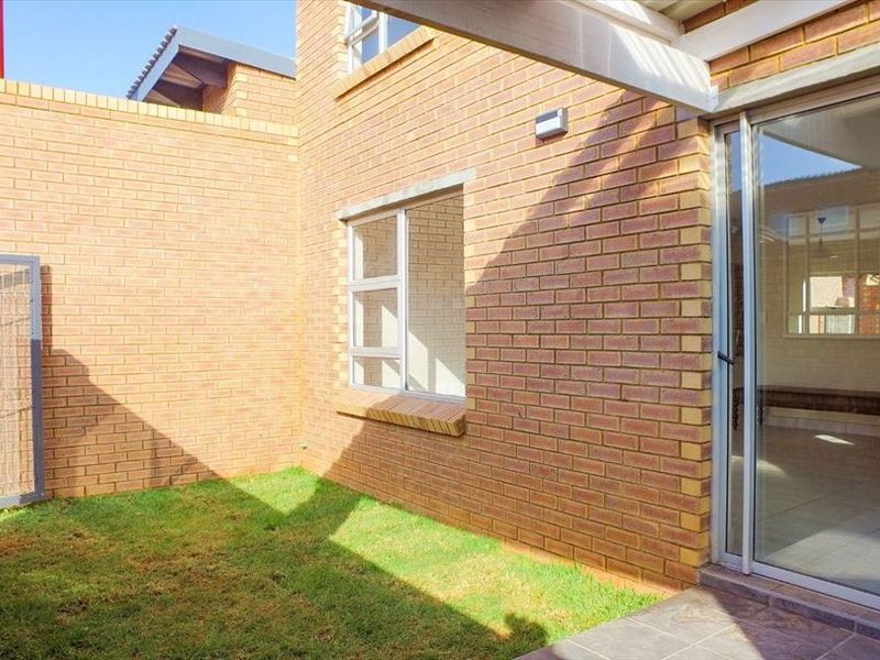 A private rear courtyard featuring face brick walls, a small lawn area, and a sliding glass door providing access to the interior living space.