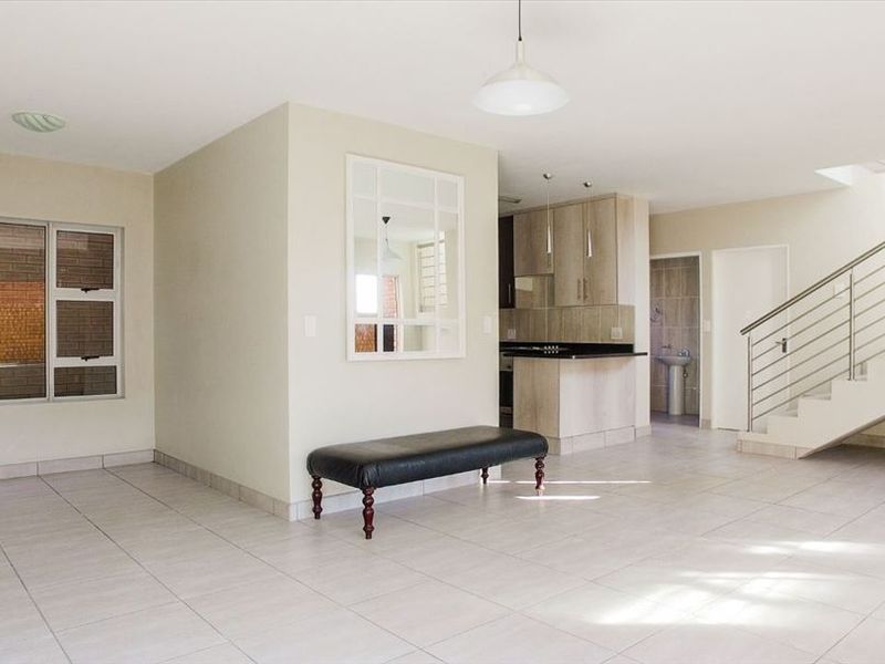 Spacious open-plan living area featuring tiled floors, a modern staircase with stainless steel balustrades, and an integrated kitchen with granite countertops.