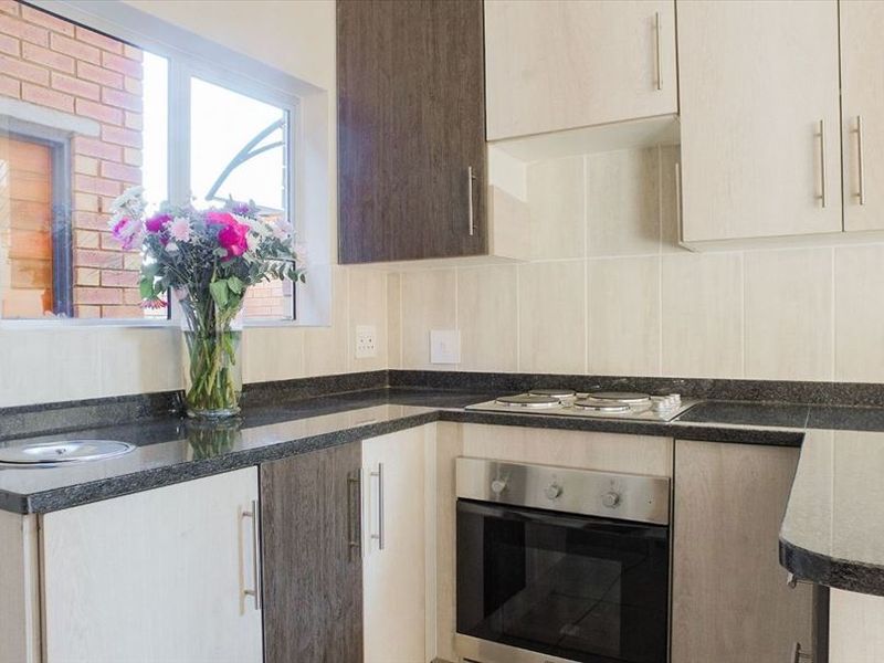 A functional kitchen featuring modern two-tone cabinetry, granite countertops, a built-in electric oven and hob, and a tiled backsplash.