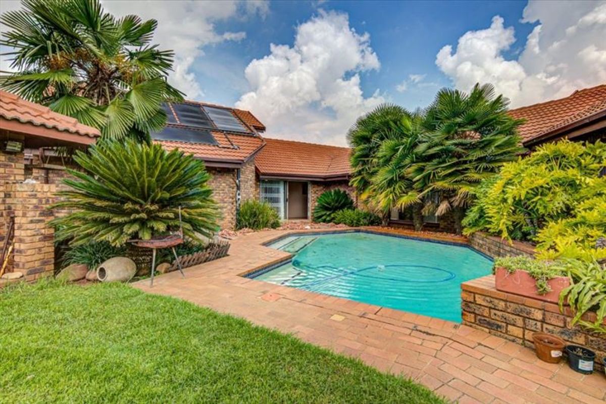 Outdoor pool area featuring a swimming pool with brick paving, surrounded by established landscaping and a face brick home with solar panels.