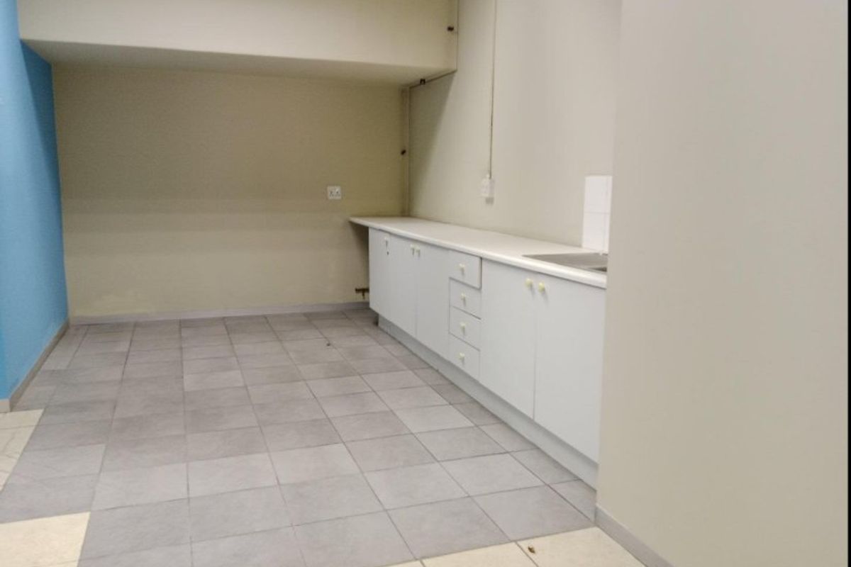 A basic commercial kitchenette featuring white built-in cabinetry, a laminate countertop with an integrated sink, and tiled flooring.