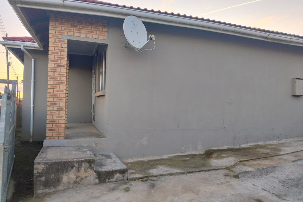 Rear exterior view of the house featuring a brick pillar, concrete steps, and a concrete apron with visible signs of wear and weathering.