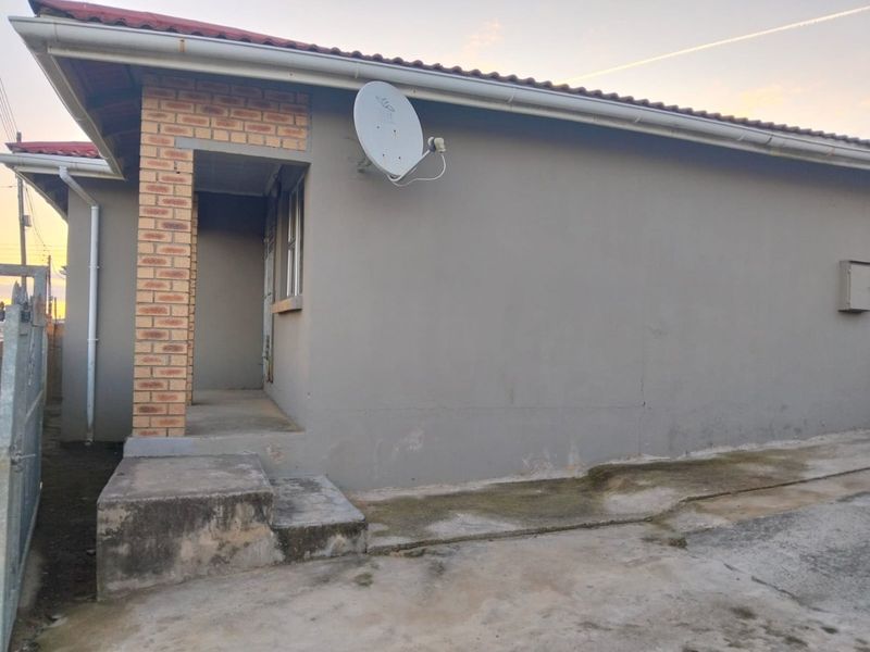 Rear exterior view of the house featuring a brick pillar, concrete steps, and a concrete apron with visible signs of wear and weathering.