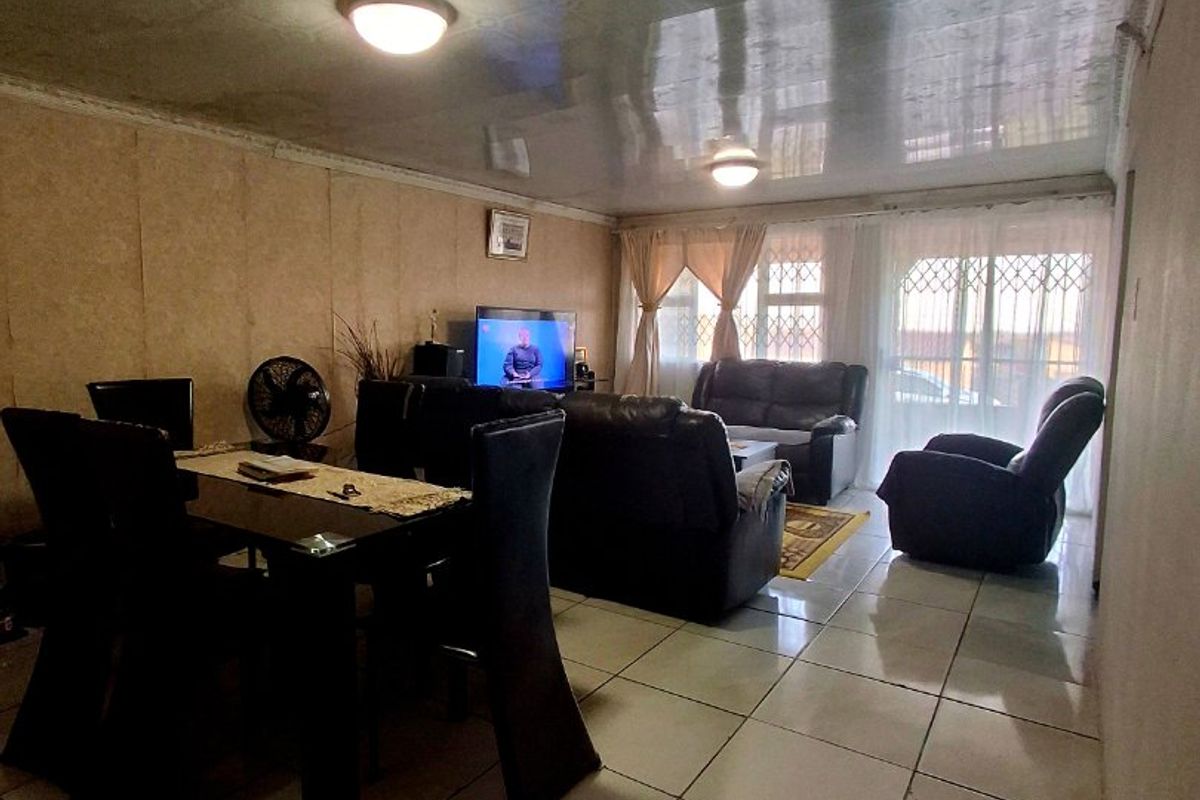 A living room featuring tiled flooring, glossy ceiling panels, and a sliding door with security gate access to the exterior.