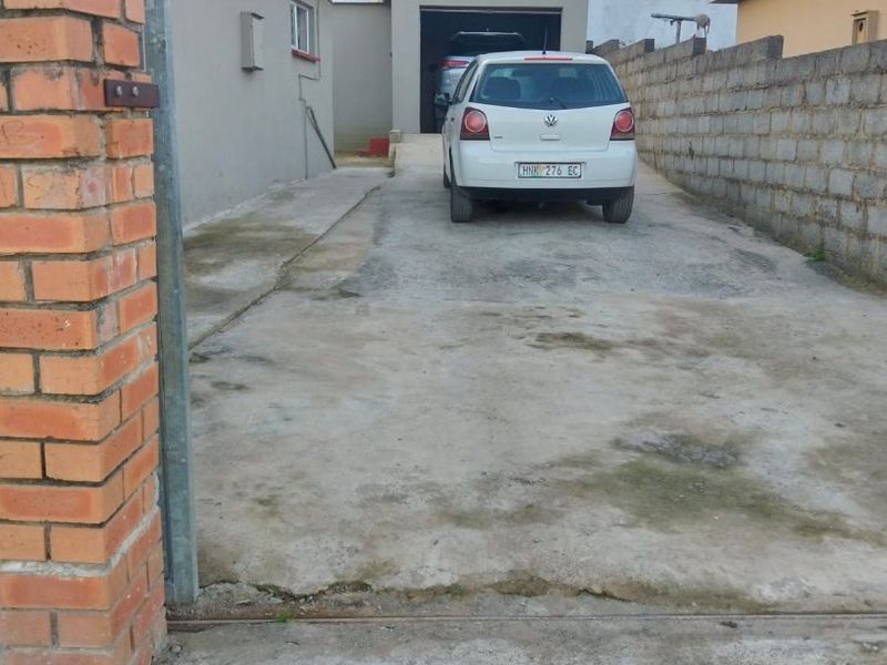 Front exterior view showing a concrete driveway leading to a garage, flanked by brick and concrete block boundary walls.