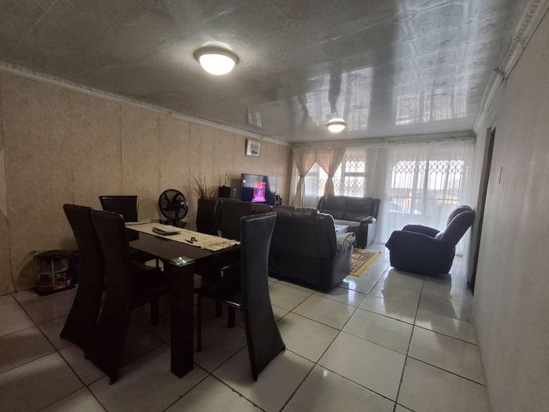 Open-plan living and dining area featuring tiled flooring, a glossy ceiling finish, and access to the exterior via a sliding glass door with security gate.