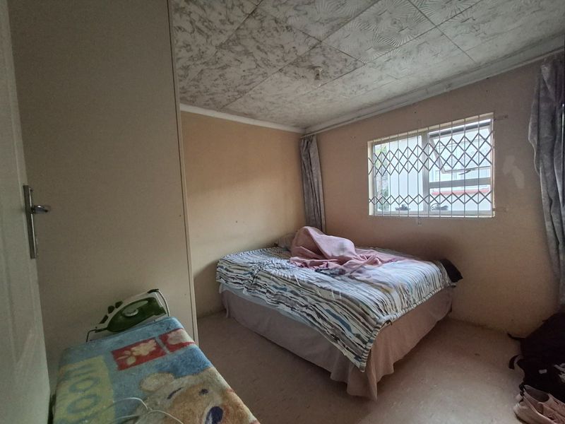 A bedroom featuring a built-in wardrobe, security gate on the window, and textured ceiling tiles, requiring cosmetic updates to improve its overall condition.