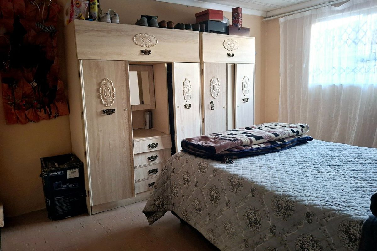 A bedroom featuring a built-in wardrobe unit, neutral wall tones, and a window with sheer curtains.