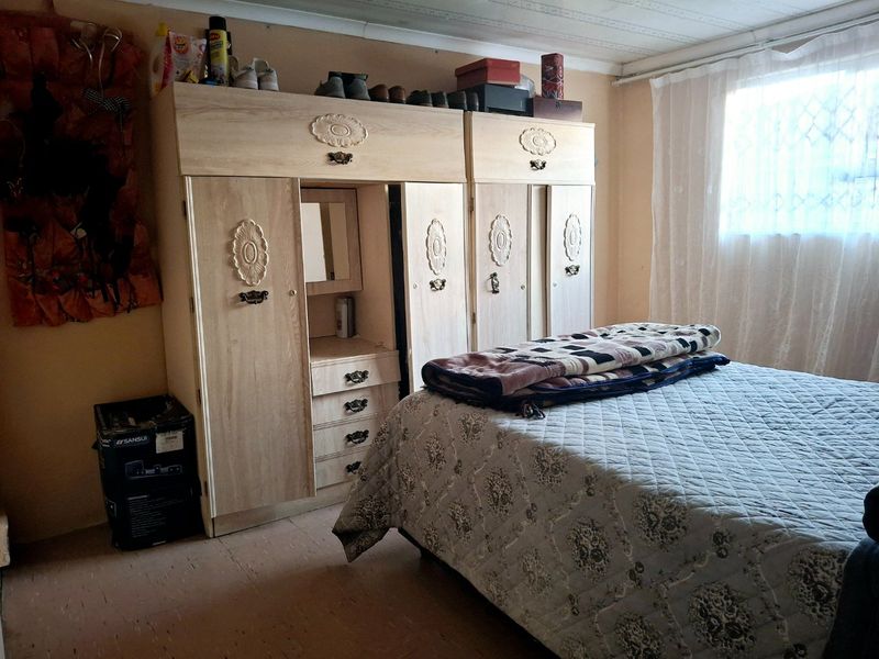 A bedroom featuring a built-in wardrobe unit, neutral wall tones, and a window with sheer curtains.