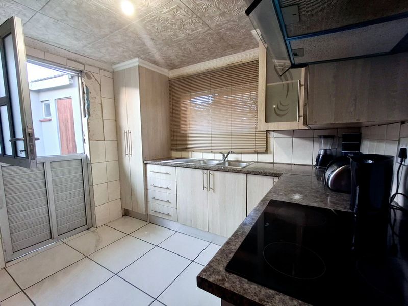 A functional kitchen featuring built-in cabinetry, laminate countertops, an electric hob, and direct access to the exterior, requiring some cosmetic repairs to walls and finishes.