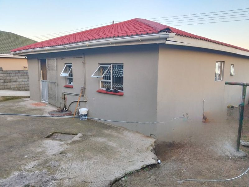 Rear view of a detached house featuring a tiled roof, security bars on windows, and a concrete apron requiring maintenance.