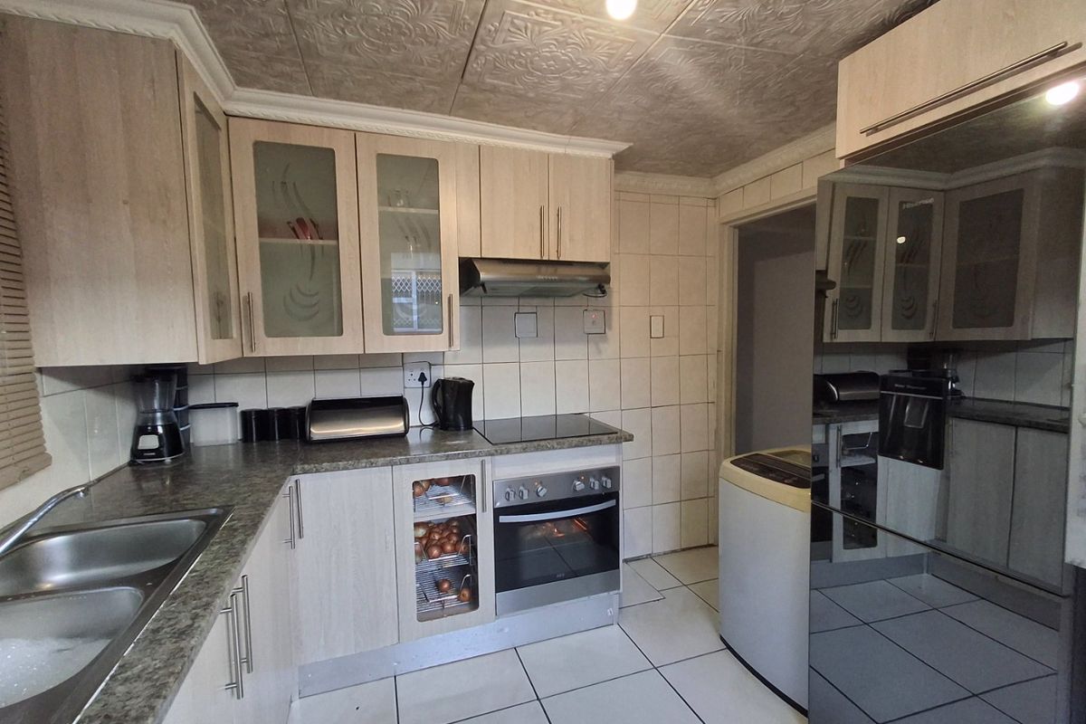 Functional kitchen featuring light wood-finish cabinetry, laminate countertops, built-in oven with hob, extractor fan, and tiled finishes throughout.