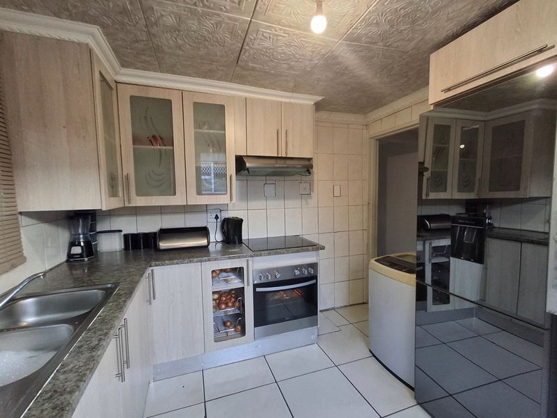 Functional kitchen featuring light wood-finish cabinetry, laminate countertops, built-in oven with hob, extractor fan, and tiled finishes throughout.