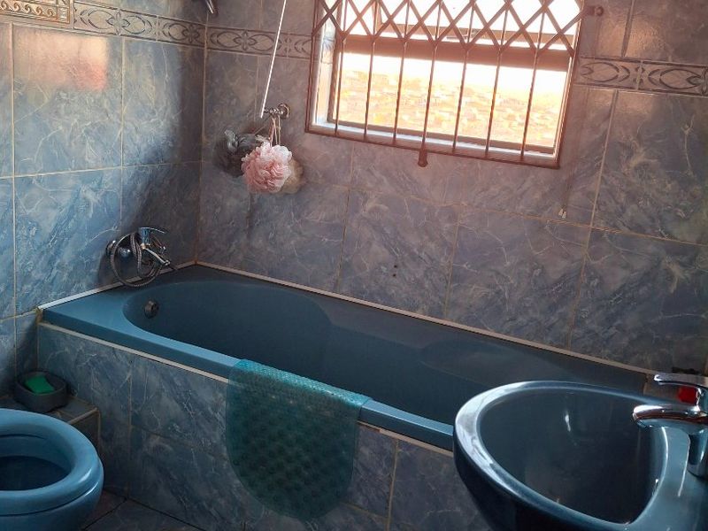 A dated bathroom featuring a blue suite, tiled walls, and a window with a security gate.