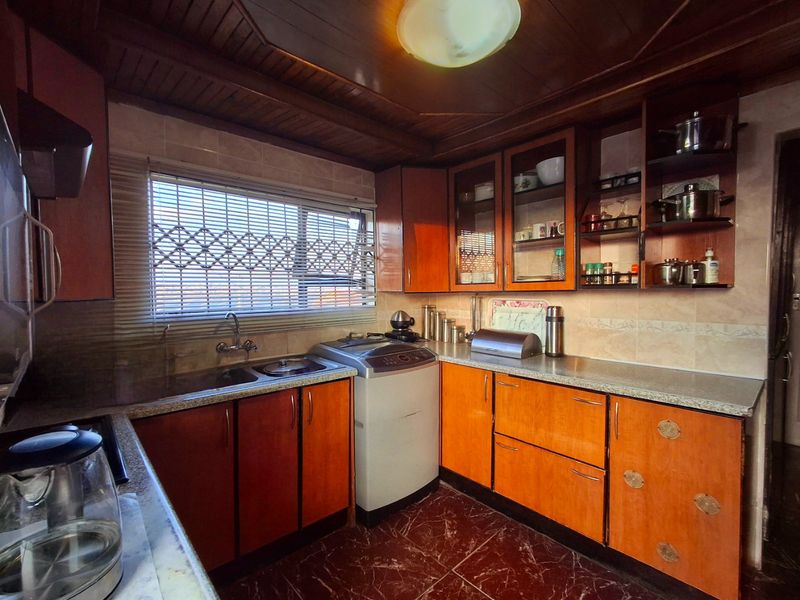 A functional kitchen featuring timber cabinetry, laminate countertops, tiled splashbacks, and a timber ceiling, offering a traditional aesthetic with potential for modern updates.