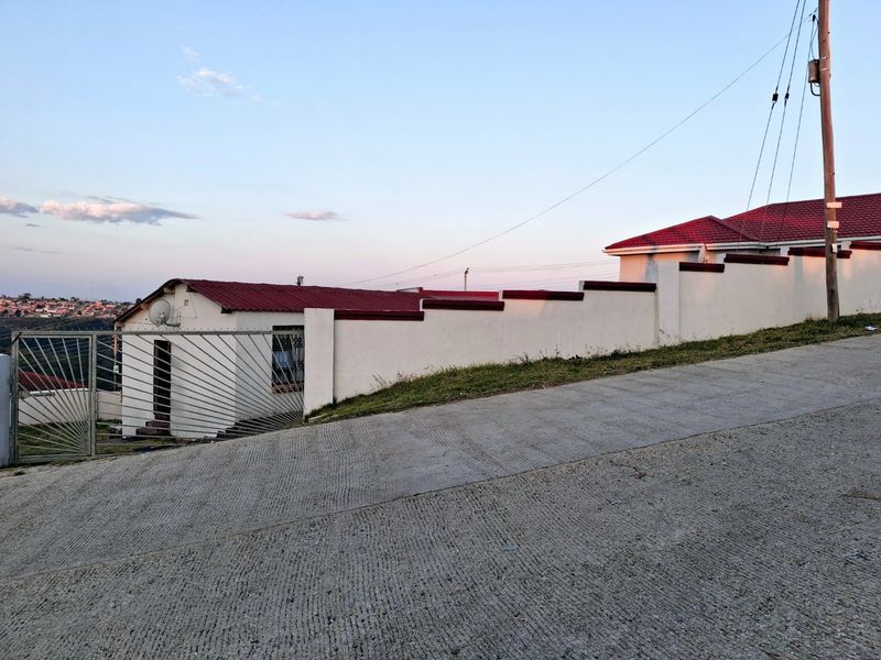 Front exterior view of the property featuring a concrete driveway, perimeter boundary wall, and metal security gate.