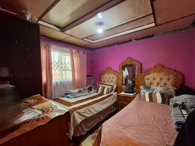 A bedroom featuring a coffered ceiling and a window with security bars, requiring cosmetic updates to improve the overall aesthetic and condition.