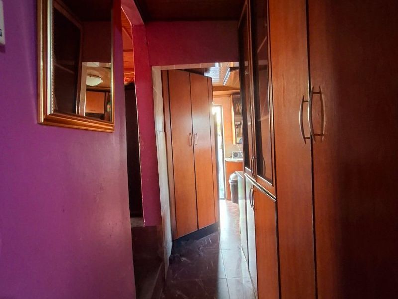 A narrow hallway featuring built-in wooden cabinetry, timber ceiling paneling, and tiled flooring, leading towards an adjacent room.