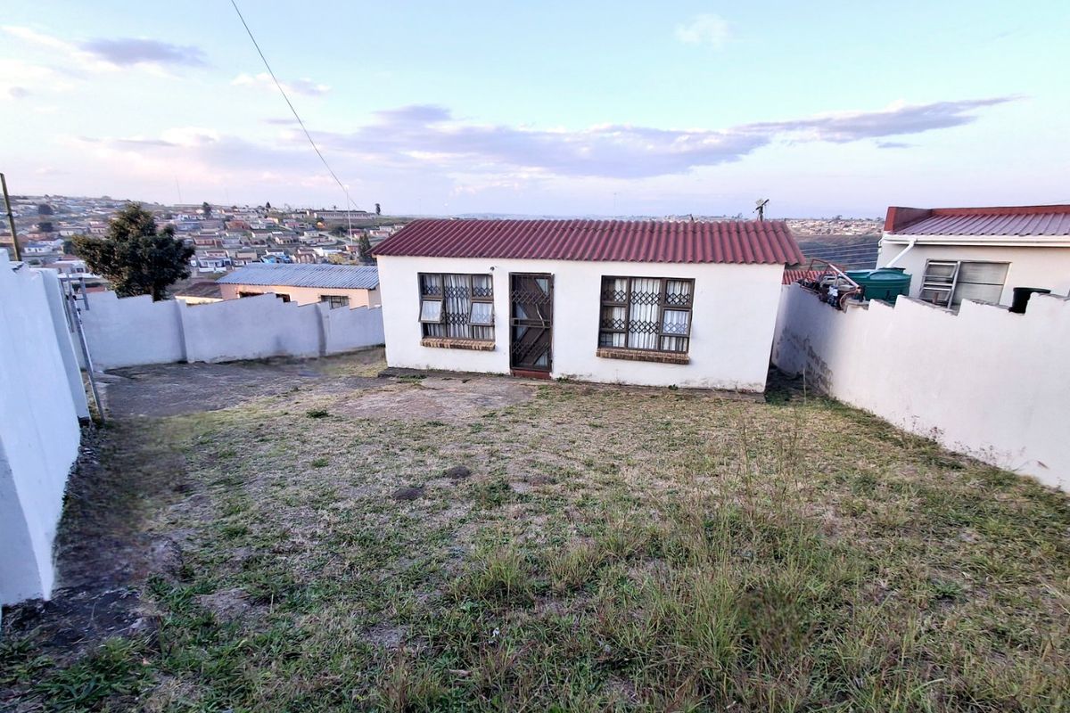 Rear view of a detached house featuring a tiled roof, security bars on windows, and a large backyard enclosed by a perimeter wall.
