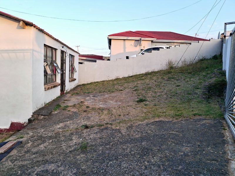 Rear exterior view showing a concrete driveway, boundary wall, and side access to the dwelling with security features installed on windows and doors.