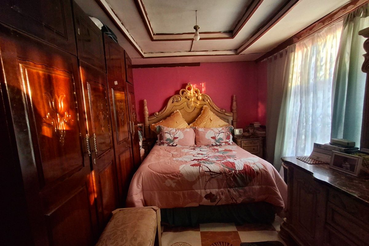 A bedroom featuring a large built-in wooden wardrobe, a coffered ceiling, and tiled flooring, offering a dated aesthetic ready for modernization.