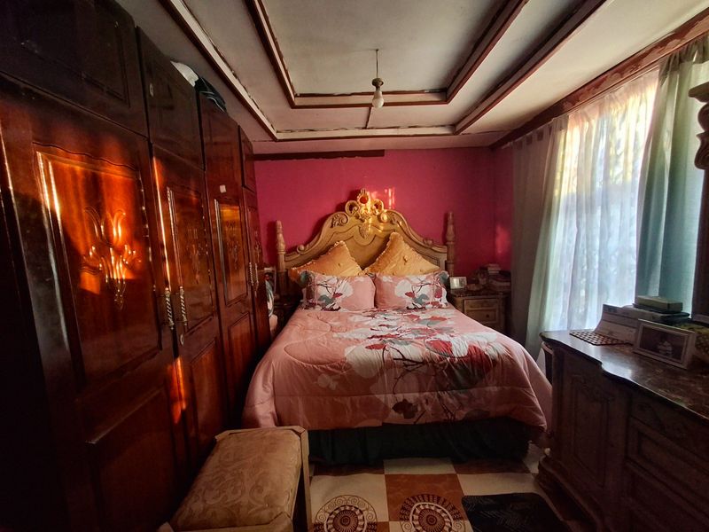 A bedroom featuring a large built-in wooden wardrobe, a coffered ceiling, and tiled flooring, offering a dated aesthetic ready for modernization.