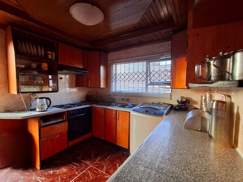 A functional kitchen featuring timber ceiling paneling, built-in cabinetry, integrated oven and hob, and tiled flooring, offering potential for a modern renovation.