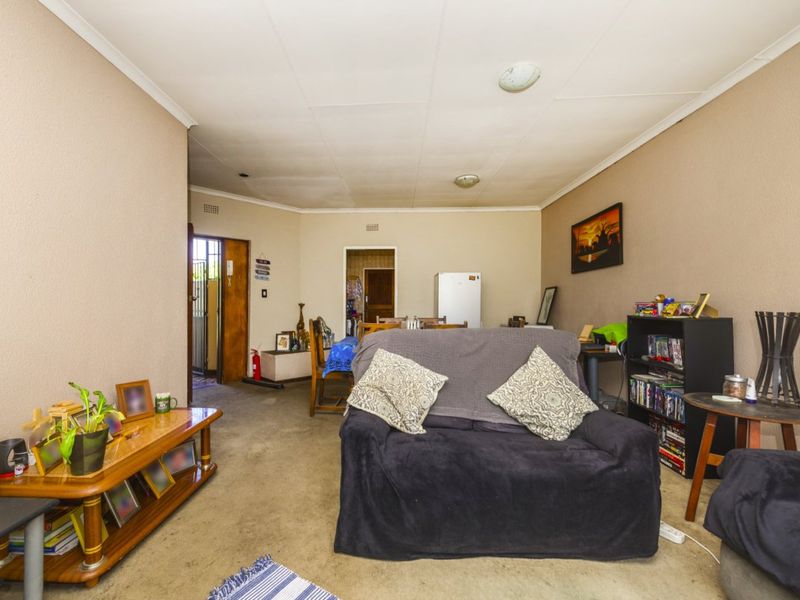 Open plan living area featuring neutral wall tones, ceiling cornices, and carpeted flooring, providing a functional space with potential for modernization.