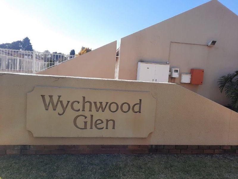 Entrance signage and boundary wall for Wychwood Glen townhouse complex, featuring security fencing and exterior utility infrastructure.