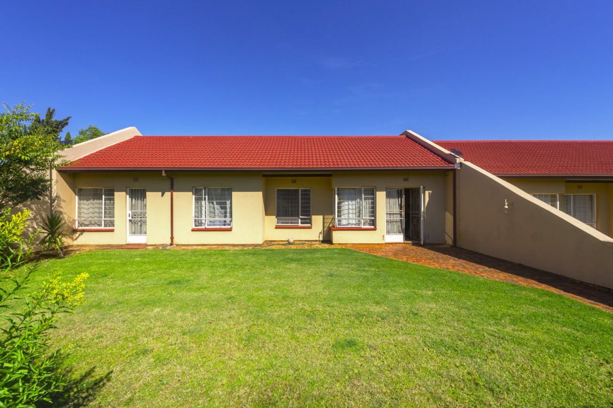 Rear view of the townhouse featuring a red tiled roof, paved walkway, and a well-maintained private lawn area.