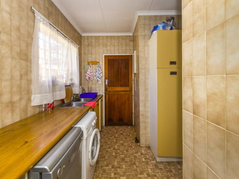 A functional scullery area featuring tiled walls, a timber countertop, stainless steel sink, and built-in cabinetry with direct access to an exterior door.